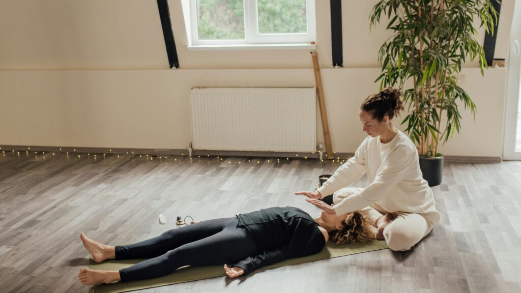 pexels-photo-6998269-6998269 A serene indoor scene of a Reiki healing session with two women on a yoga mat for relaxation and wellness.